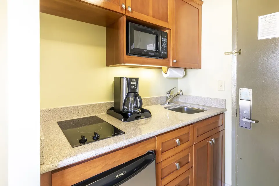 Studio Suite kitchenette with cooktop, coffee maker, sink, microwave, and cabinets at Pacific Monarch Hotel.