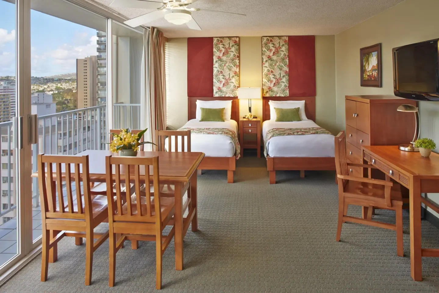 Studio suite with two twin beds, dining table, desk, TV, and balcony doors at Pacific Monarch Hotel.