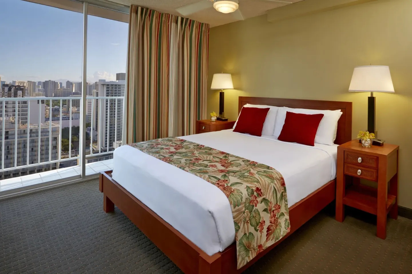 One-bedroom suite bed with red pillows and city-facing windows at Pacific Monarch Hotel.