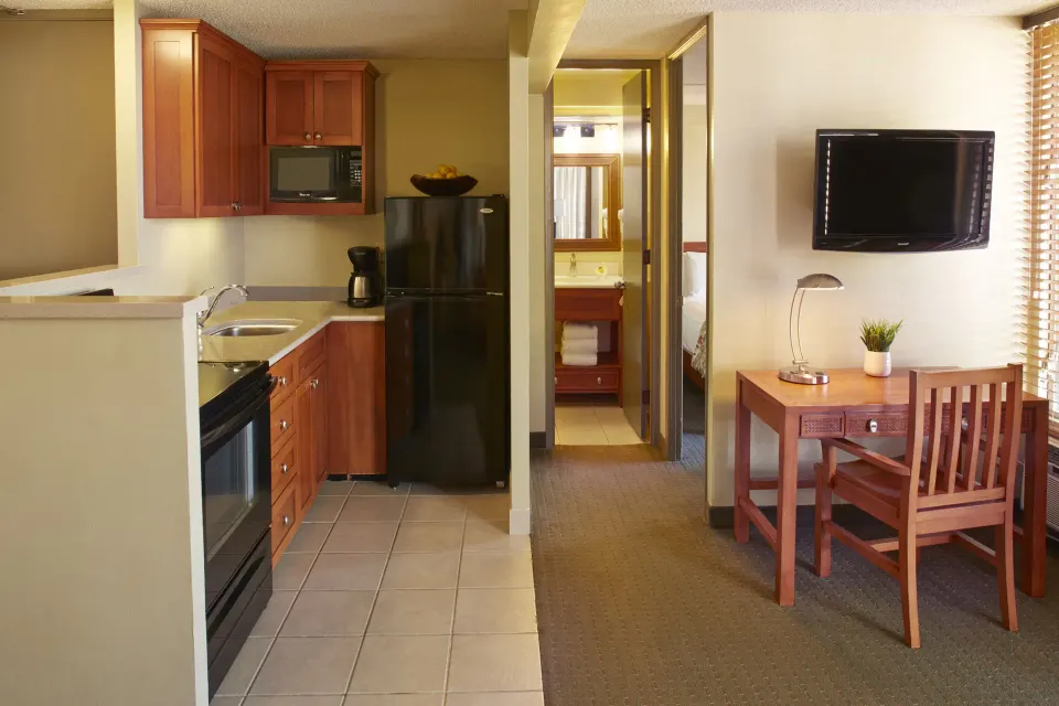 One-bedroom suite kitchenette, desk, TV, and bedroom doorway at Pacific Monarch Hotel.