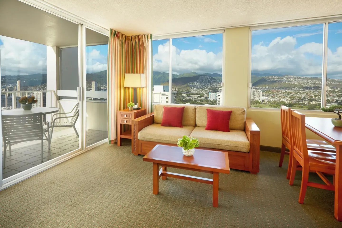 One-bedroom suite living area with sofa, desk, balcony, and mountain views at Pacific Monarch Hotel.