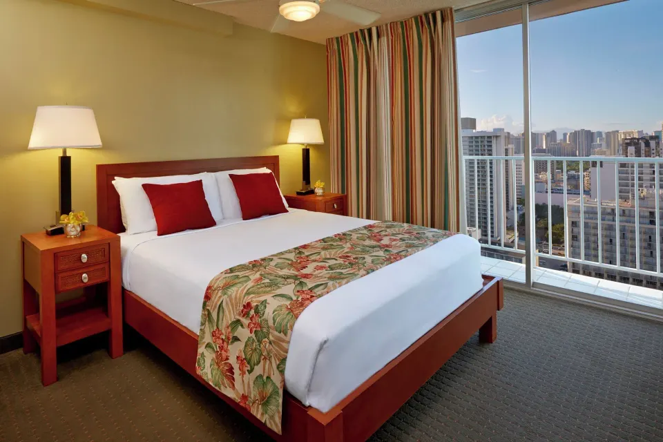 One-bedroom suite bedroom with queen bed, balcony doors, and city views at Pacific Monarch Hotel.