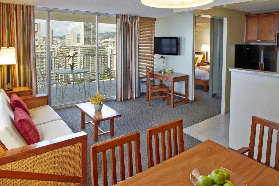 One-bedroom suite sitting area with balcony, desk, and kitchenette at Pacific Monarch Hotel.