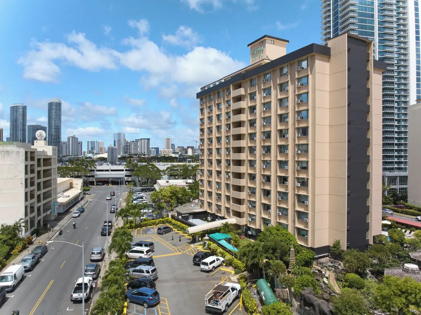 Pagoda Hotel tower with entrance drive, parking area, and city buildings.
