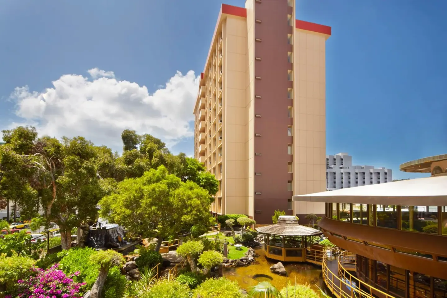 Hotel tower, garden pond, and restaurant roofline at Pagoda Hotel on a sunny day.