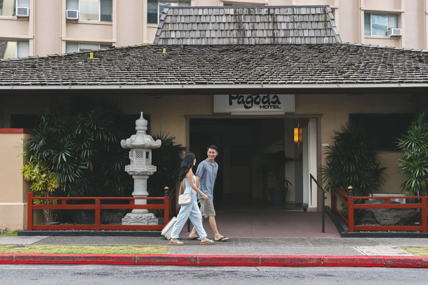 Pagoda Hotel entrance with sign, stone lantern, and guests on the sidewalk.