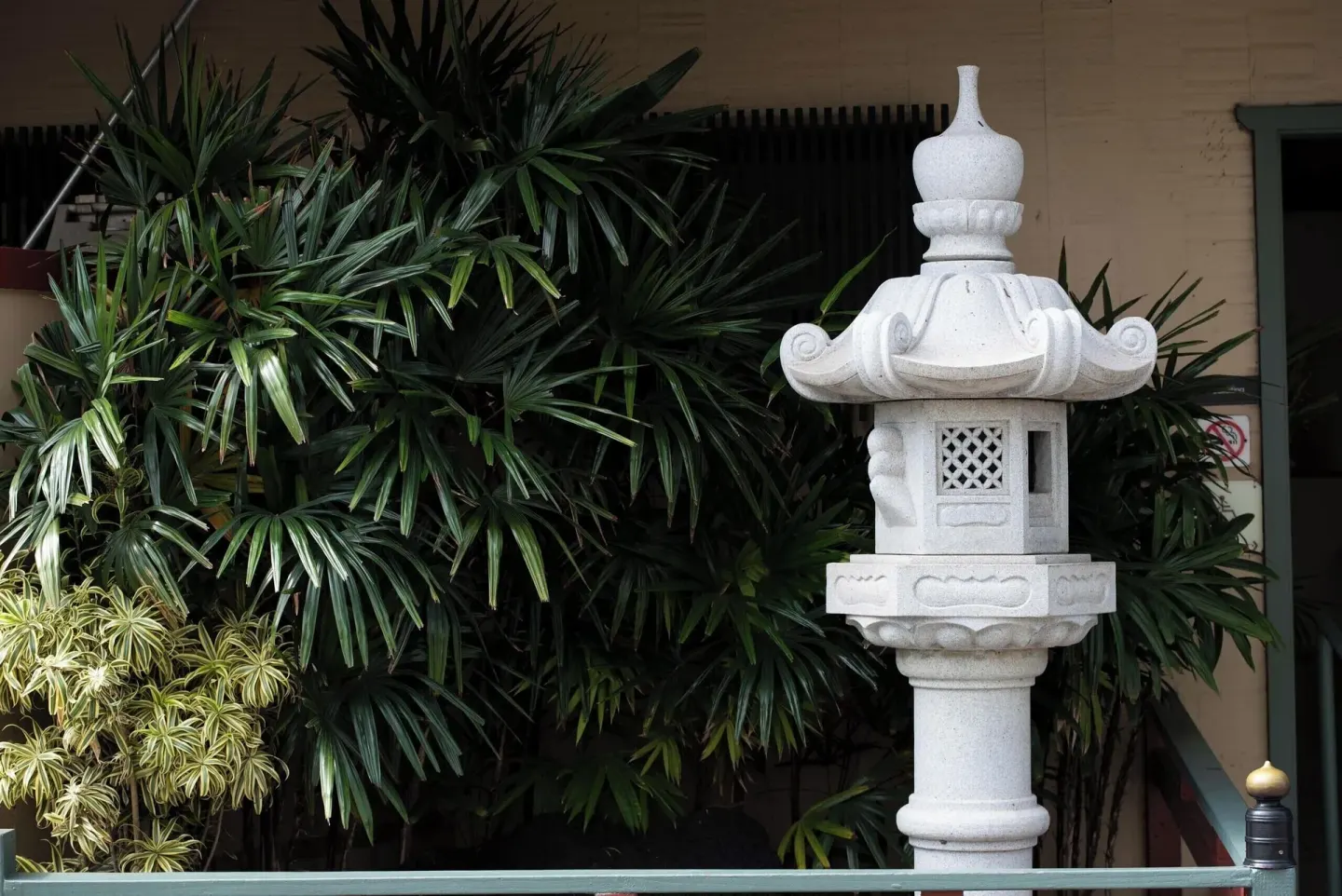 White stone lantern beside tropical foliage and railing at Pagoda Hotel.