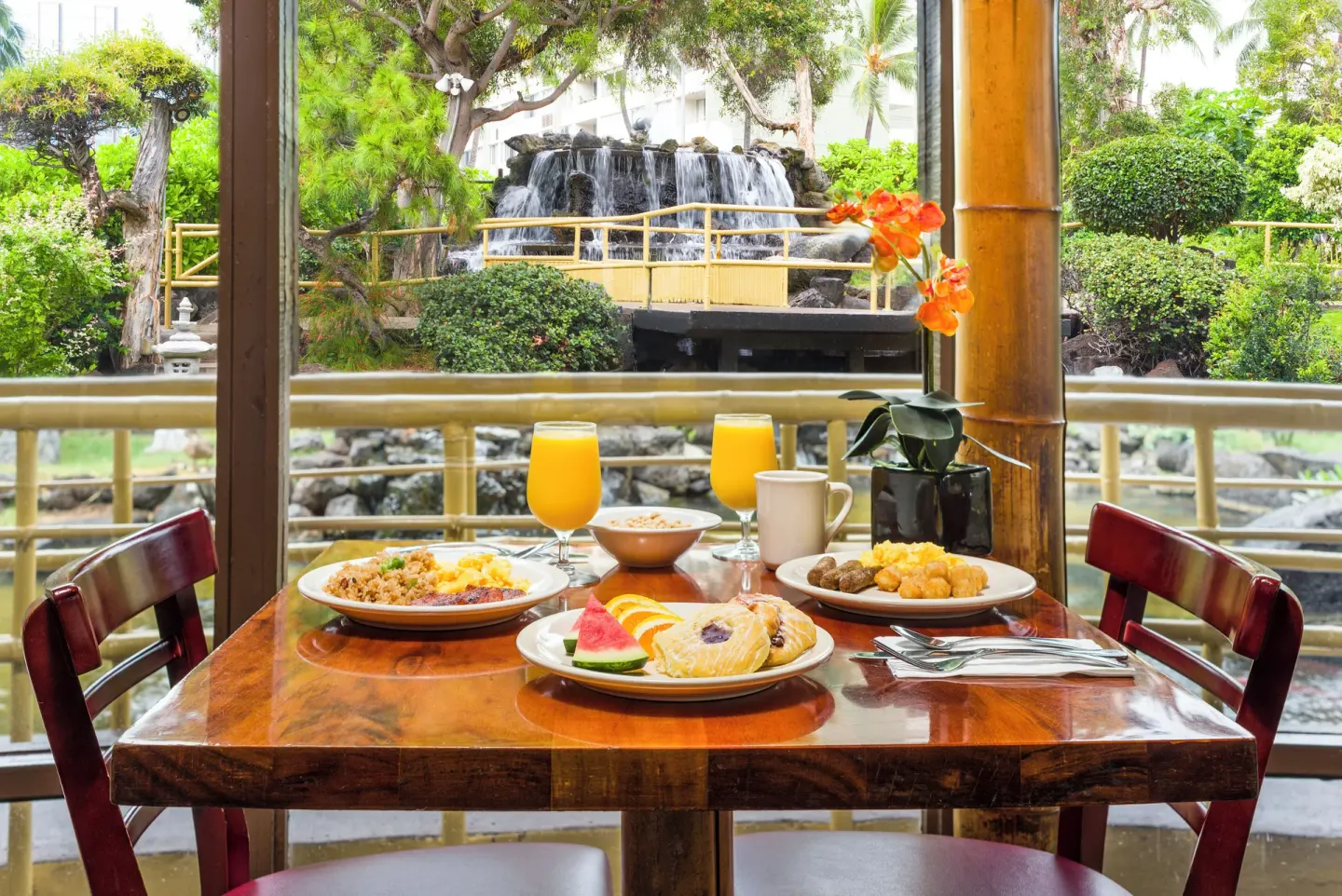 Breakfast table by the garden waterfall at Pagoda Hotel with juice, fruit, and hot plates.