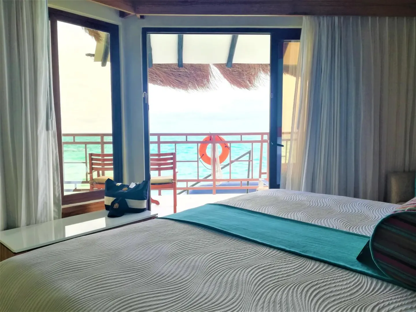 King bed facing a balcony and ocean view at Palafitos Overwater Bungalows.