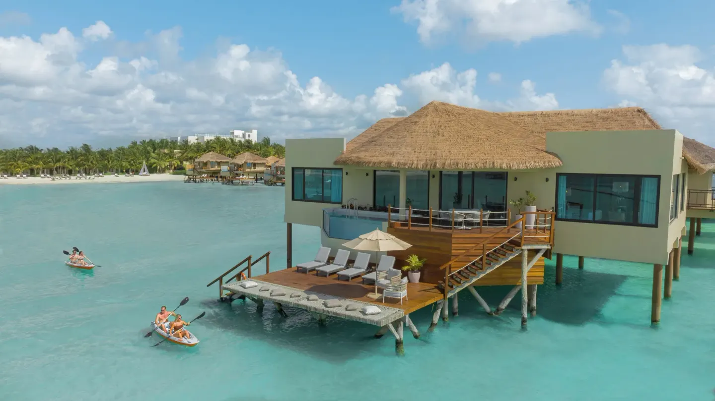 Overwater bungalow deck with lounge chairs and kayakers at Palafitos Overwater Bungalows.