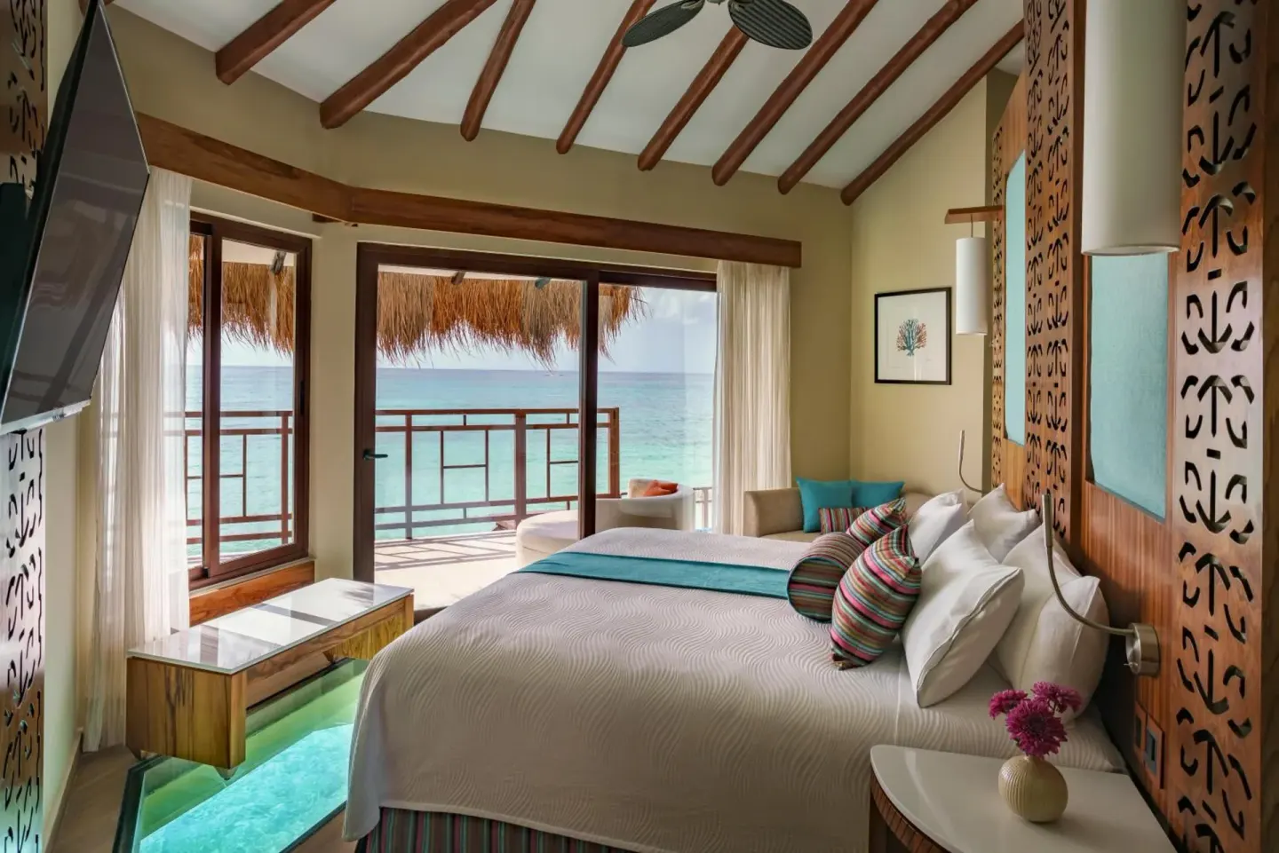 King bed facing a balcony and ocean view at Palafitos Overwater Bungalows.