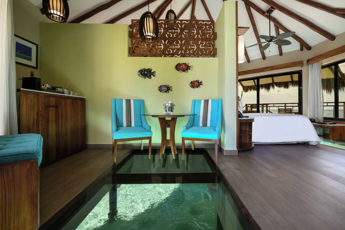 Overwater bungalow sitting area with glass floor and king bed at Palafitos Overwater Bungalows.