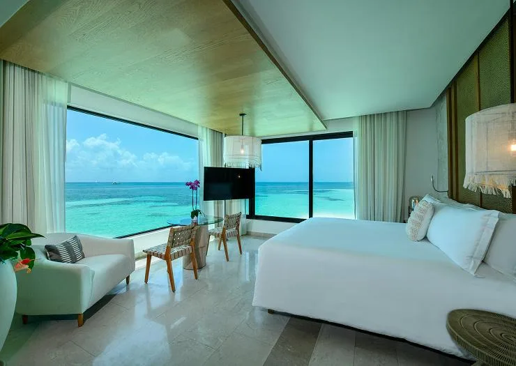 Master bedroom with a king bed and corner panoramic windows over the Caribbean in the Two Bedroom Presidential Overwater Bungalow.