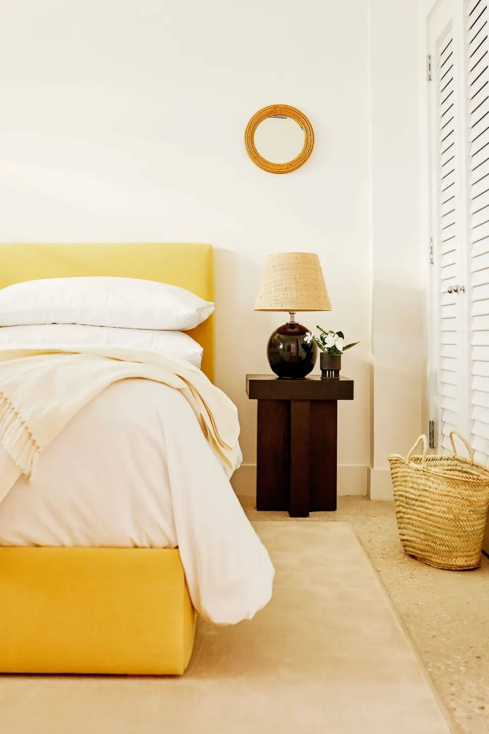 Side view of a bed with a yellow base, bedside table and woven basket at Palm Heights.