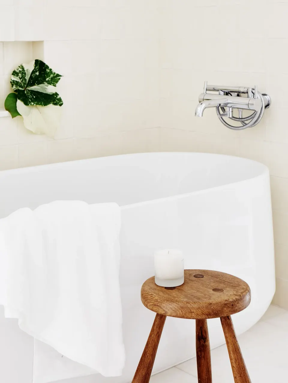 White freestanding bathtub with a wooden stool and towel at Palm Heights.