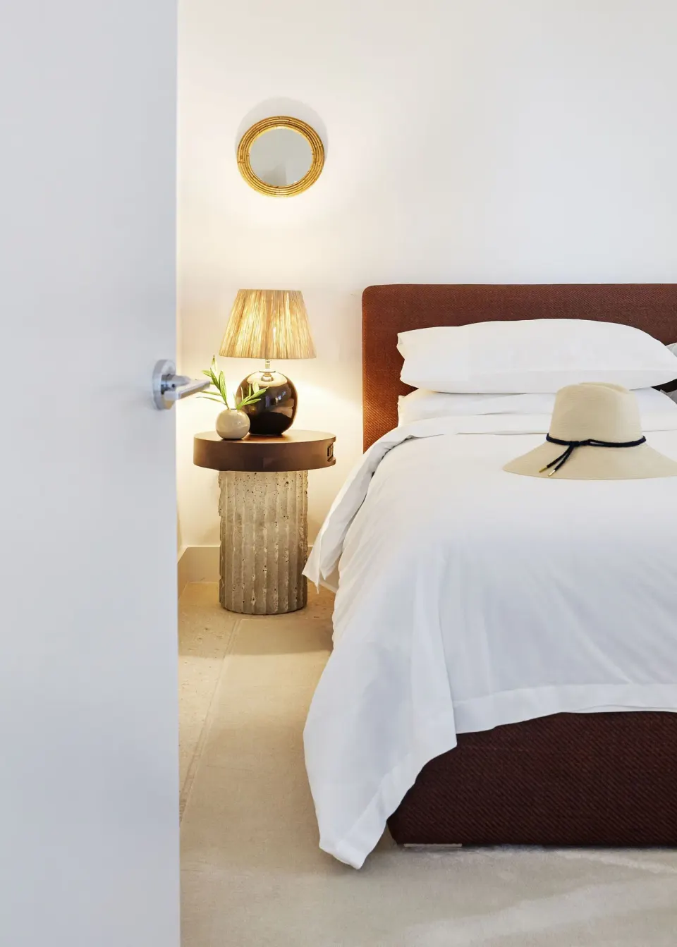 Part of a guest bedroom at Palm Heights showing a made bed, bedside table and lamp with a straw hat.
