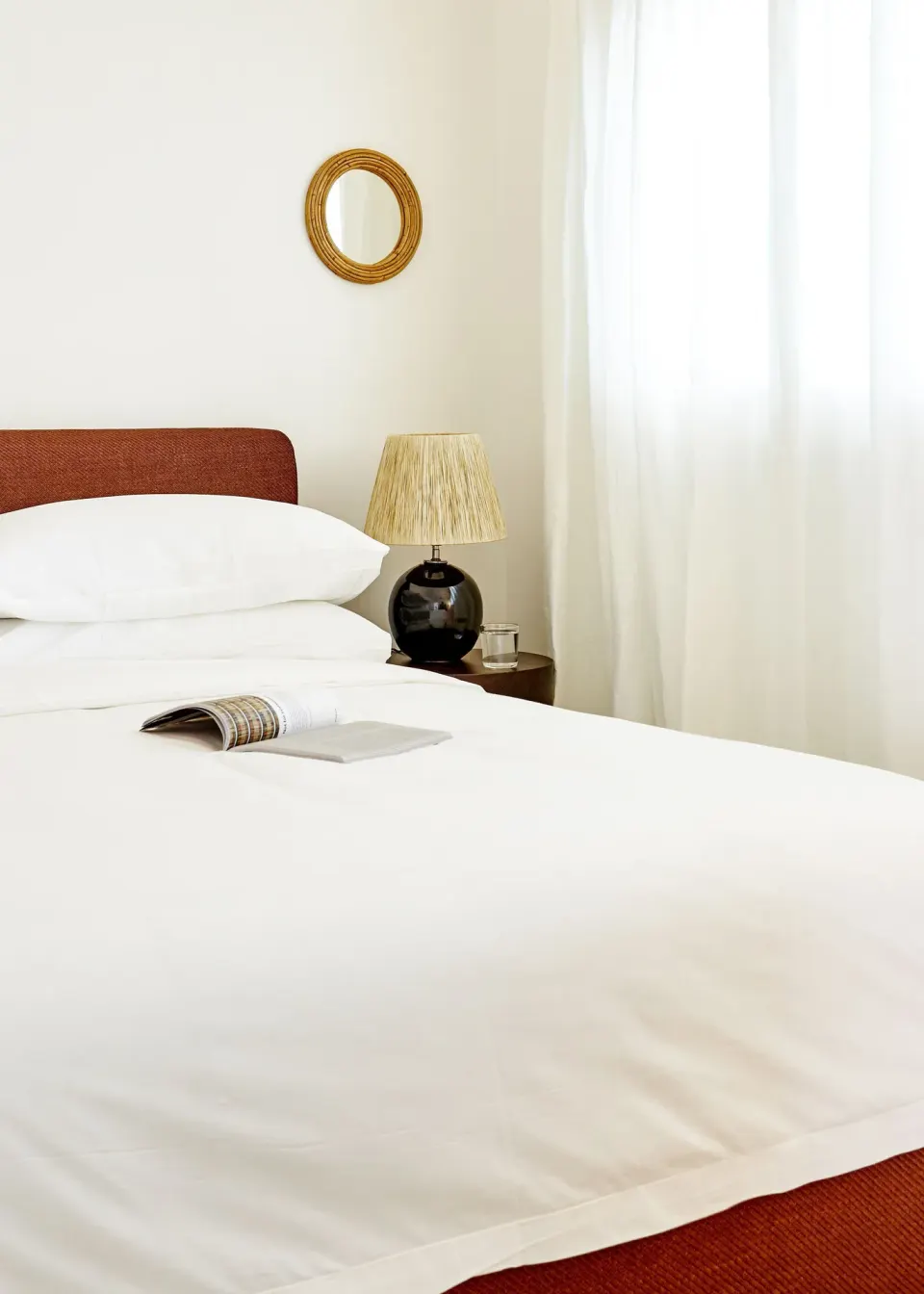 Close-up of a Palm Heights guest room king bed with bedside lamp and a small round mirror on the wall.