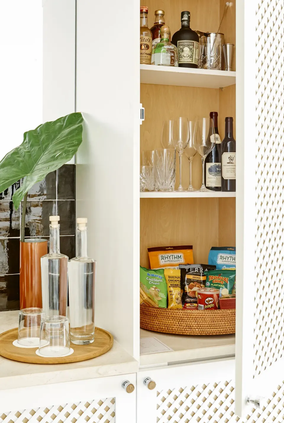Open minibar cabinet stocked with glasses, bottles and snack baskets at Palm Heights.