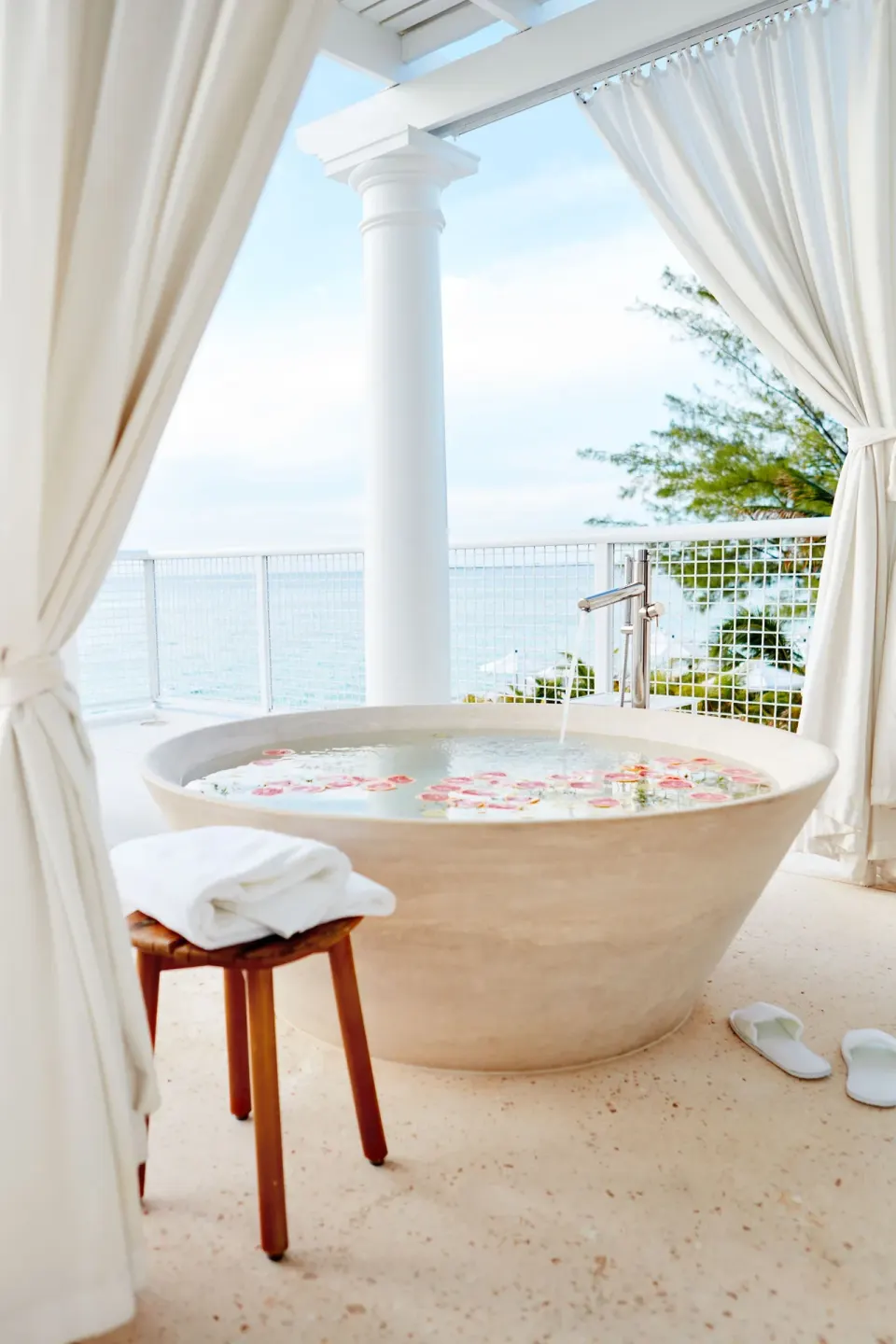 Outdoor round soaking tub with ocean view framed by curtains at Palm Heights