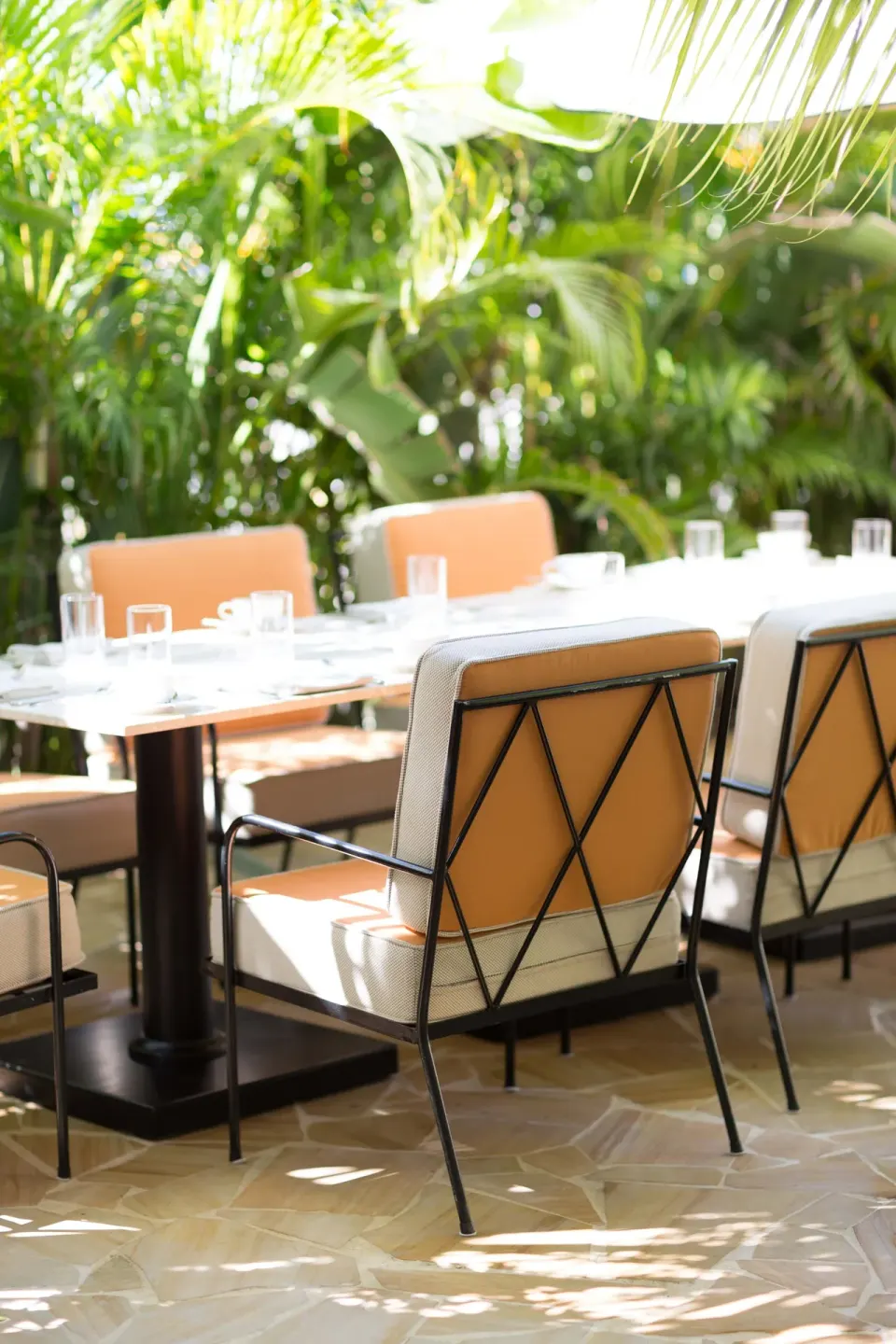 Outdoor dining table with orange chairs and tropical plants at Palm Heights