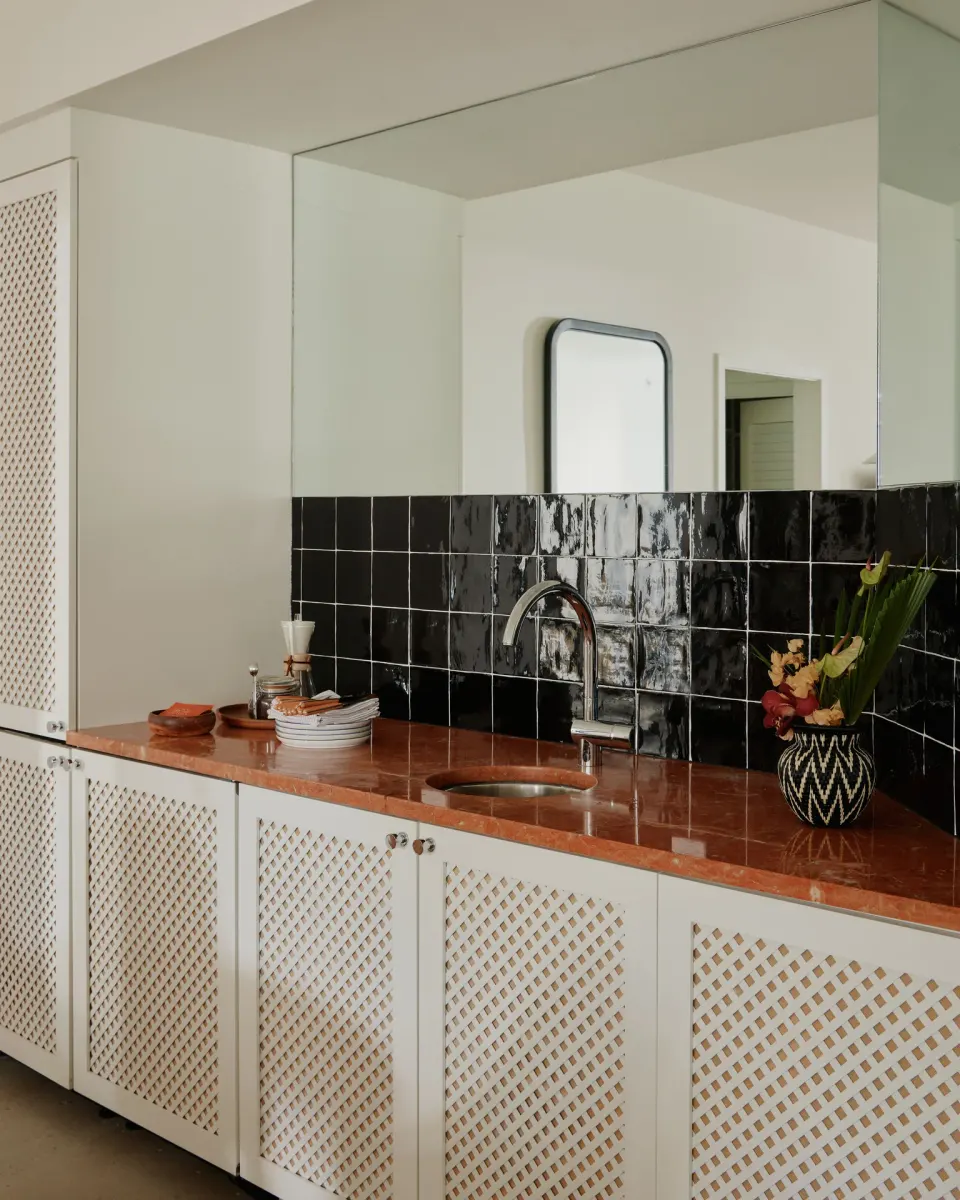 Kitchenette at Palm Heights with a terracotta countertop, black tiled splashback and sink.