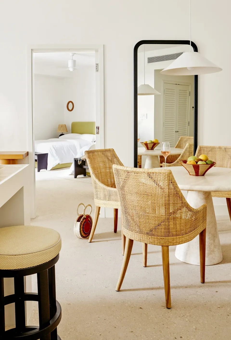 Open-plan dining space at Palm Heights with rattan chairs, round table and a view into a bedroom.