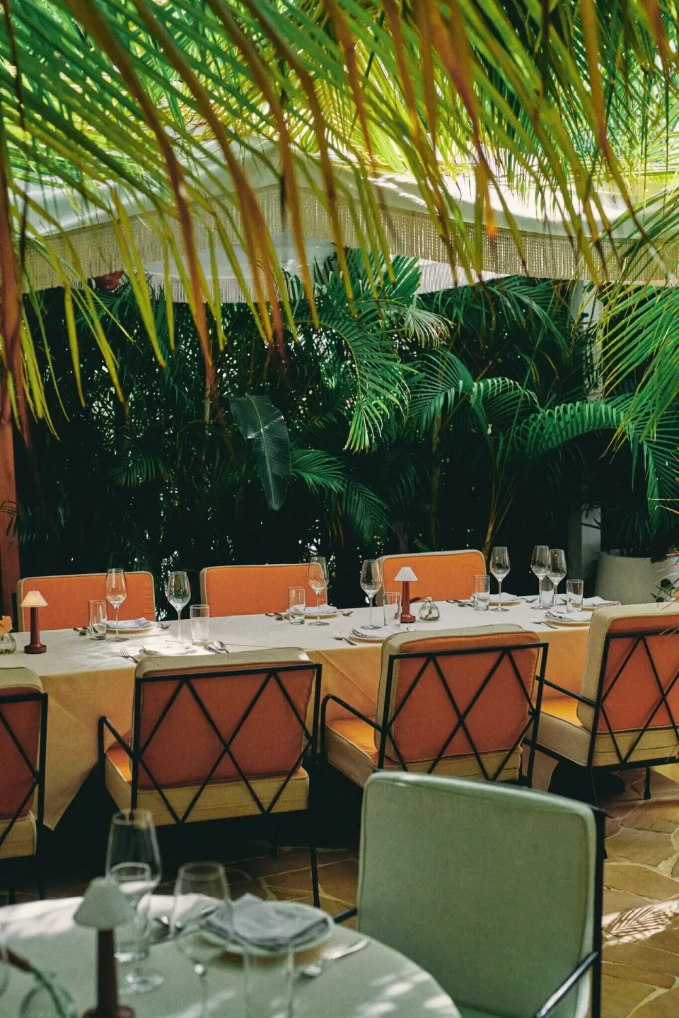 Shaded outdoor dining table with orange chairs and tropical palms at Palm Heights