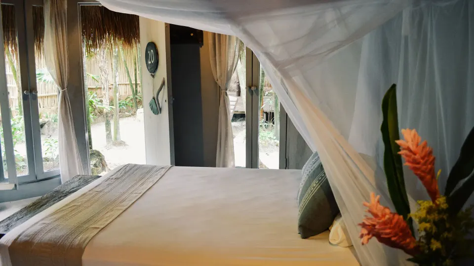 King bed with layered pillows and wood floors in a bungalow at Papaya Playa Project