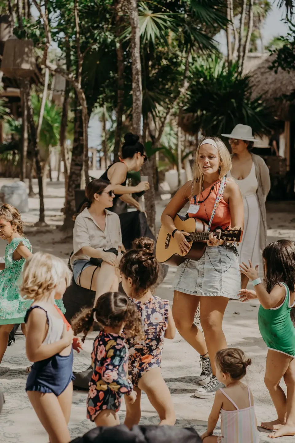 Woman playing guitar among children dancing on the sand at Papaya Playa Project