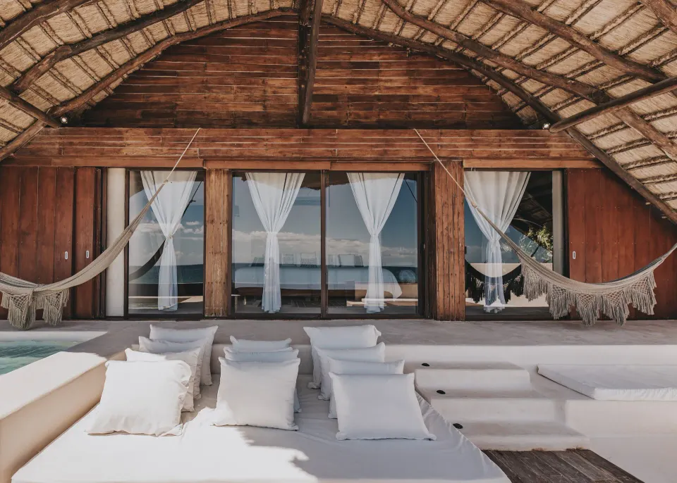 Shaded beachfront lounge with hammocks and layered daybeds at Papaya Playa Project