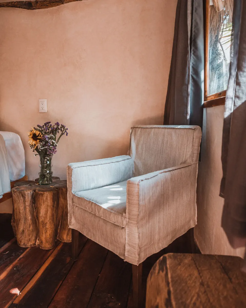 Armchair and tree-stump side table beside a window at Papaya Playa Project