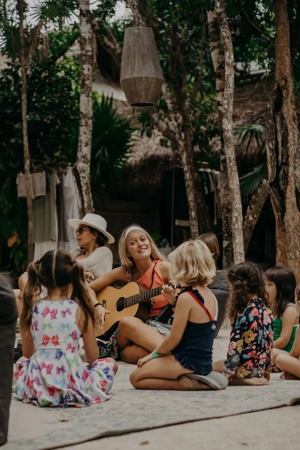 Group of children seated on the sand listening to a musician at Papaya Playa Project