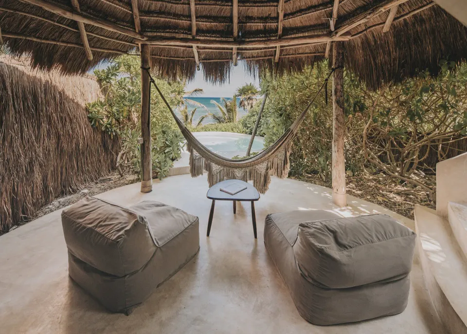 Shaded cabana with hammock, two poufs and a small pool view at Papaya Playa Project