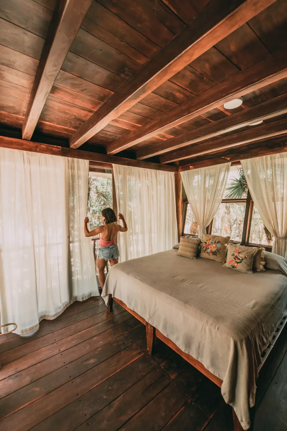 King bed with rustic beams and two chairs by the window in a guest room at Papaya Playa Project