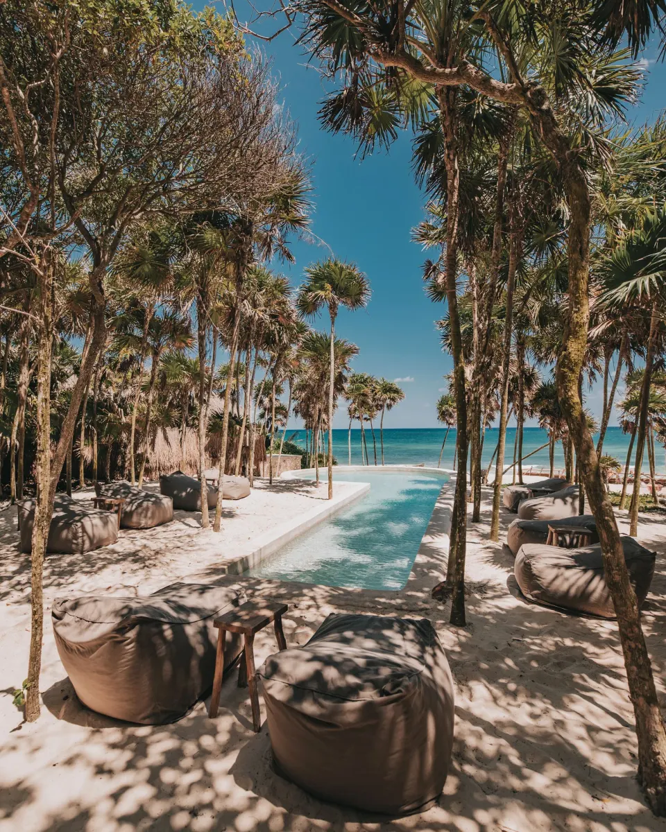 Long narrow pool framed by palms and beanbag loungers facing the ocean at Papaya Playa Project