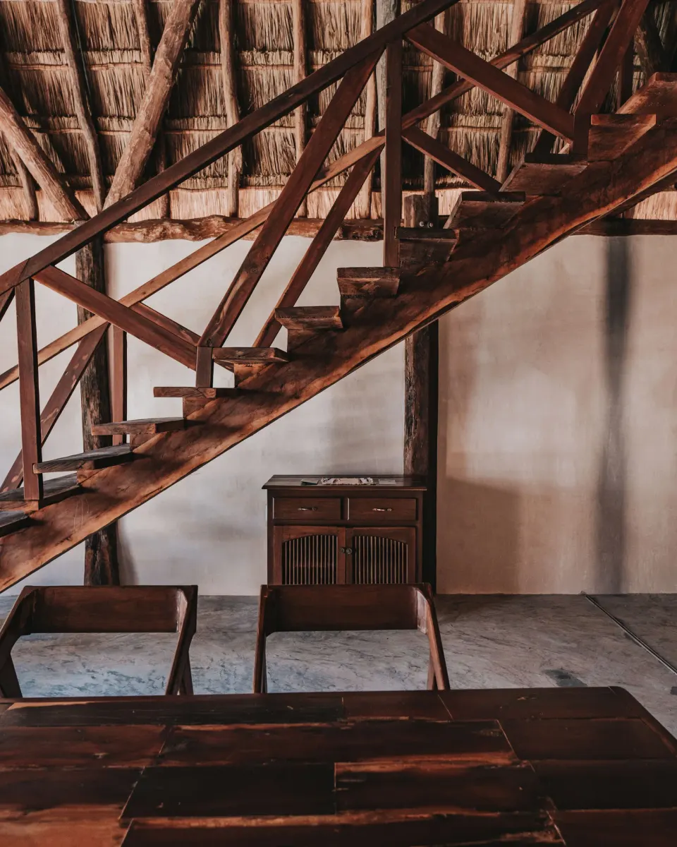 Wooden staircase and dining table beneath a thatched loft structure at Papaya Playa Project