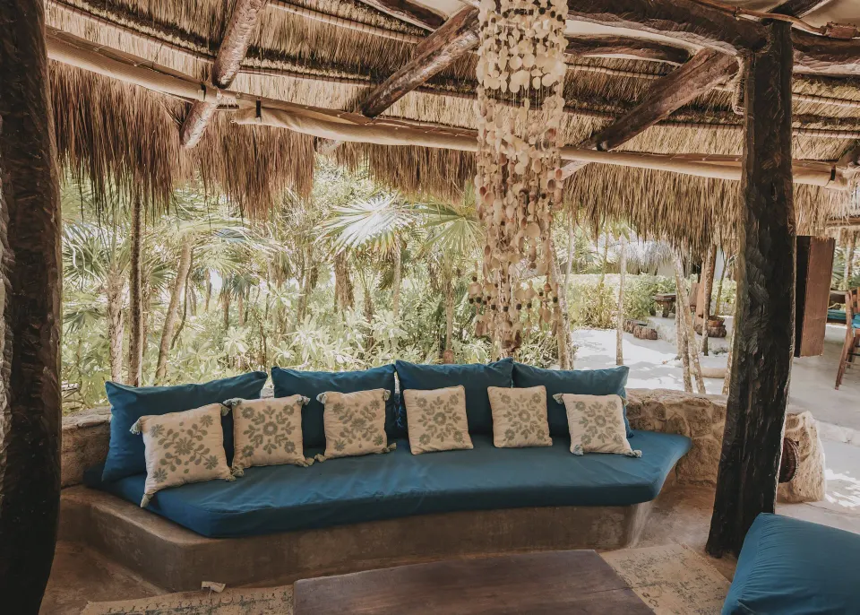 Thatched open-air lounge with blue cushions and shell chandelier at Papaya Playa Project