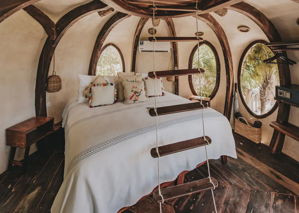 Round wooden pod bedroom with king bed and circular windows at Papaya Playa Project