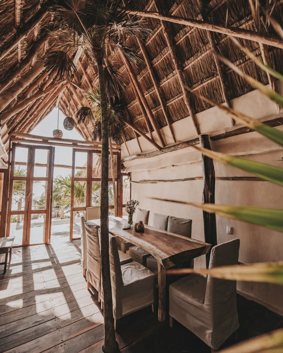Dining table under a high thatched roof at Papaya Playa Project