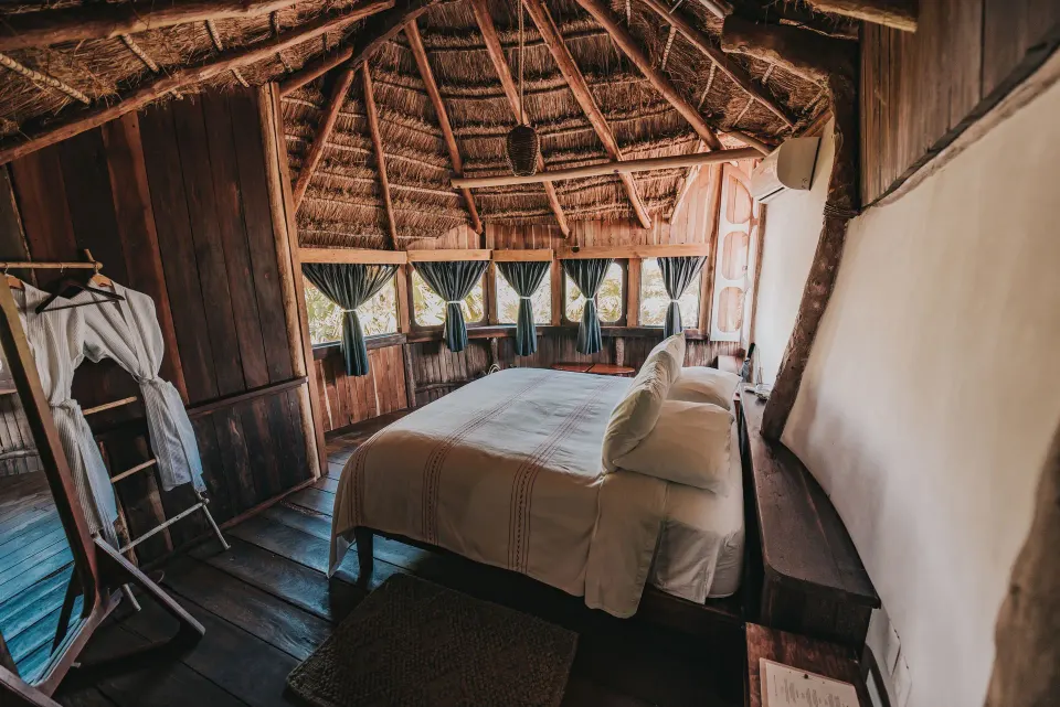 Thatched-roof bedroom with king bed and wooden floor at Papaya Playa Project.