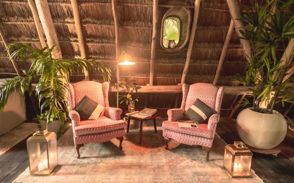Thatched-roof seating nook with two upholstered chairs at Papaya Playa Project