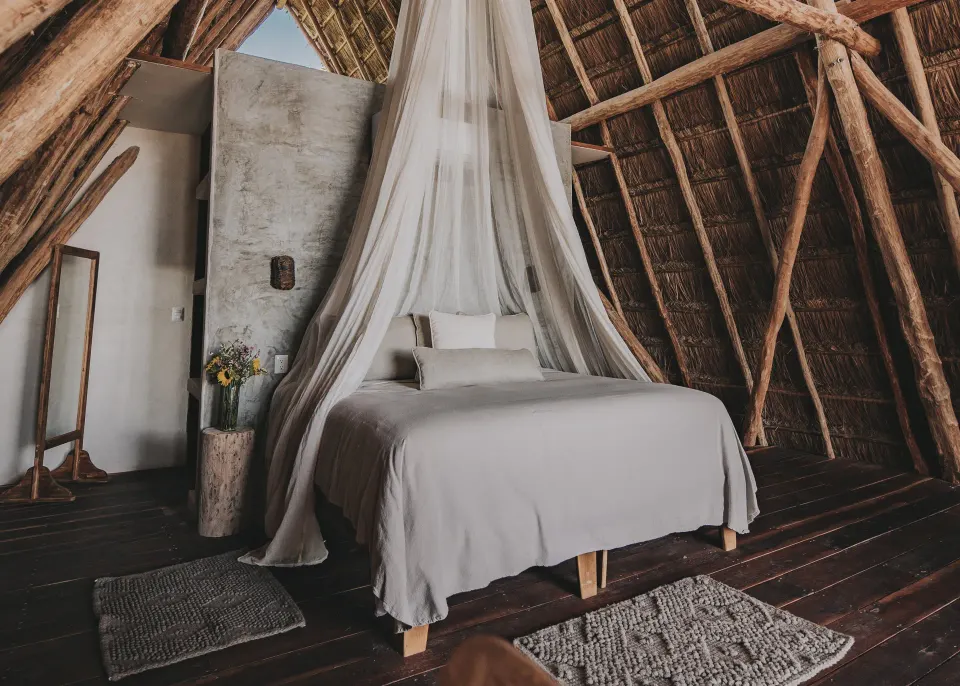 Thatched-roof suite with a canopy mosquito net over a bed at Papaya Playa Project.