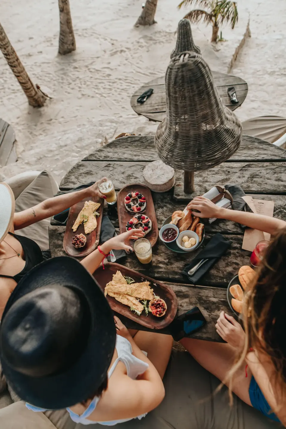 Overhead of friends sharing breakfast on a wooden table at Papaya Playa Project beach
