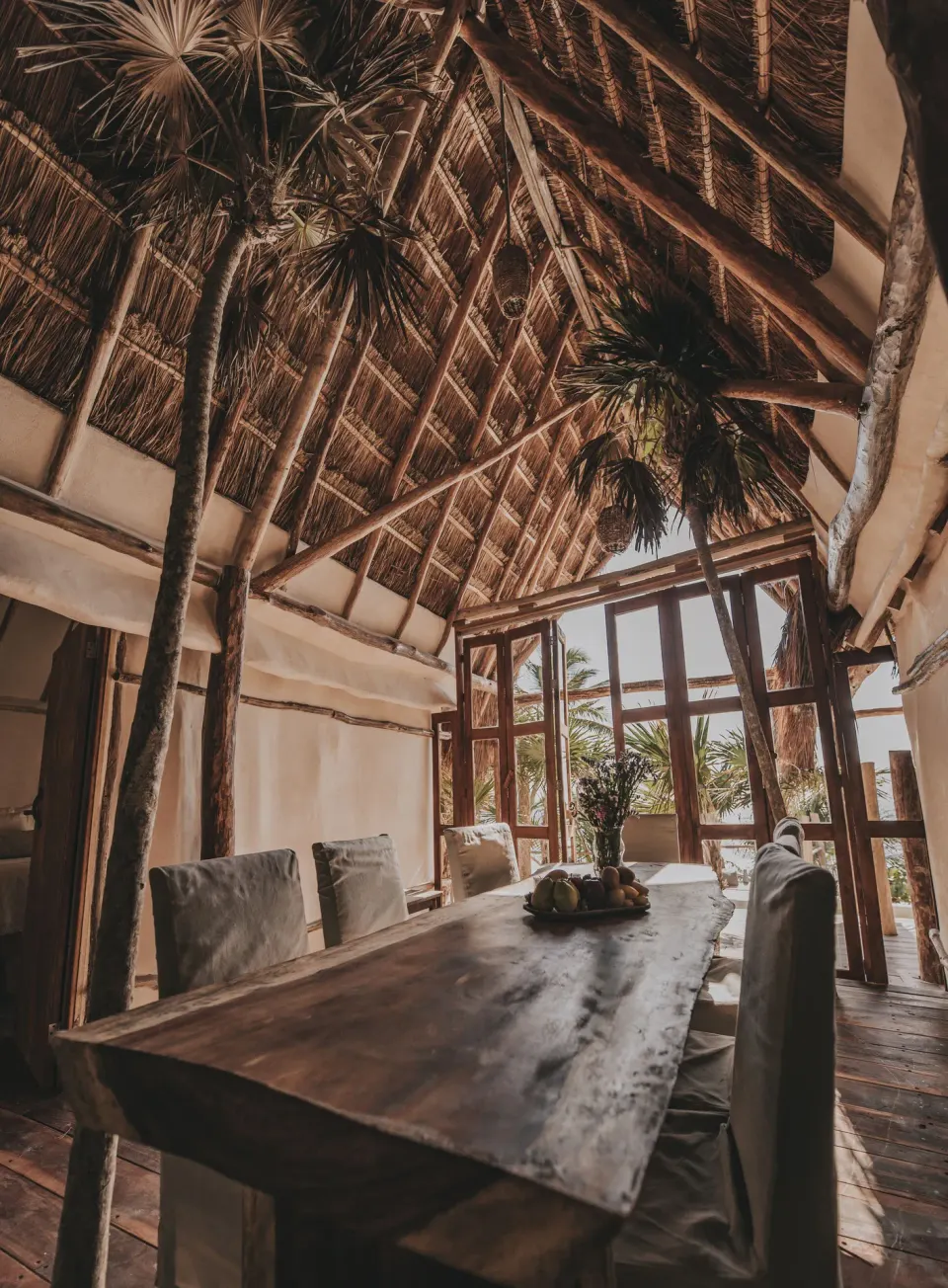 Indoor palapa dining room with large wooden table and tall thatched ceiling at Papaya Playa Project
