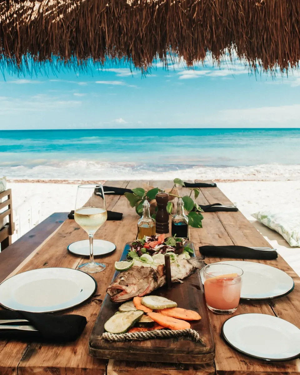 Wooden table set with a whole fish and drinks by the beach at Papaya Playa Project