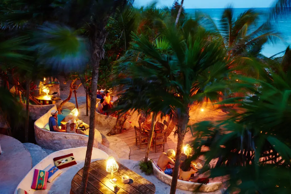 Evening view of lit outdoor lounges and palm trees at Papaya Playa Project