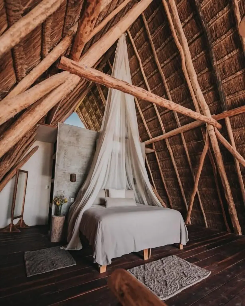 Thatched-roof loft bedroom with a canopy-draped bed at Papaya Playa Project.