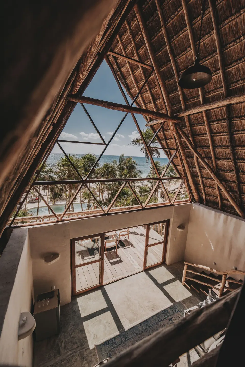 Ocean-view loft interior with triangular thatched window framing the sea at Papaya Playa Project.
