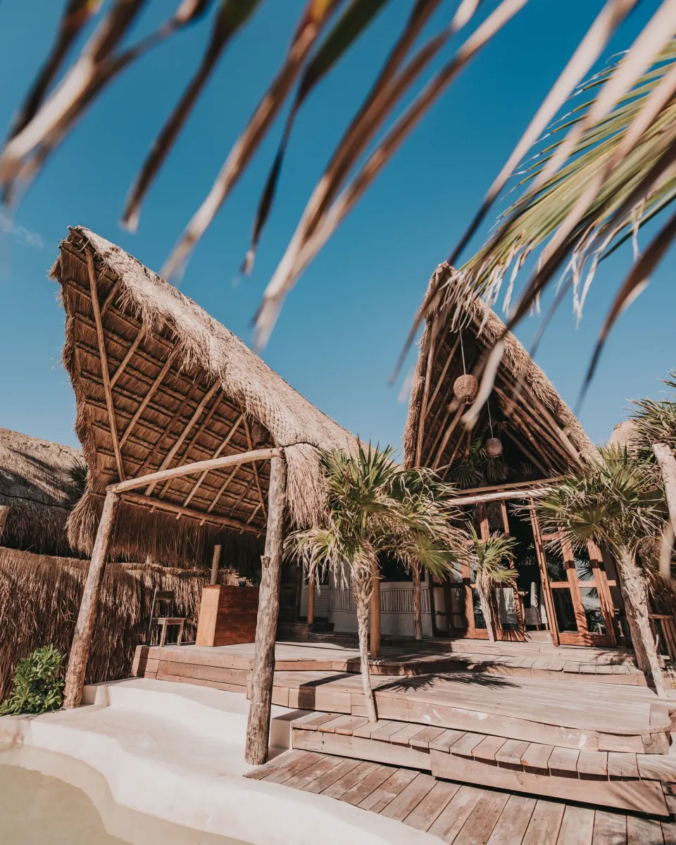 Thatched palapa peaks and wooden deck of Casa Coco against a blue sky at Papaya Playa Project.