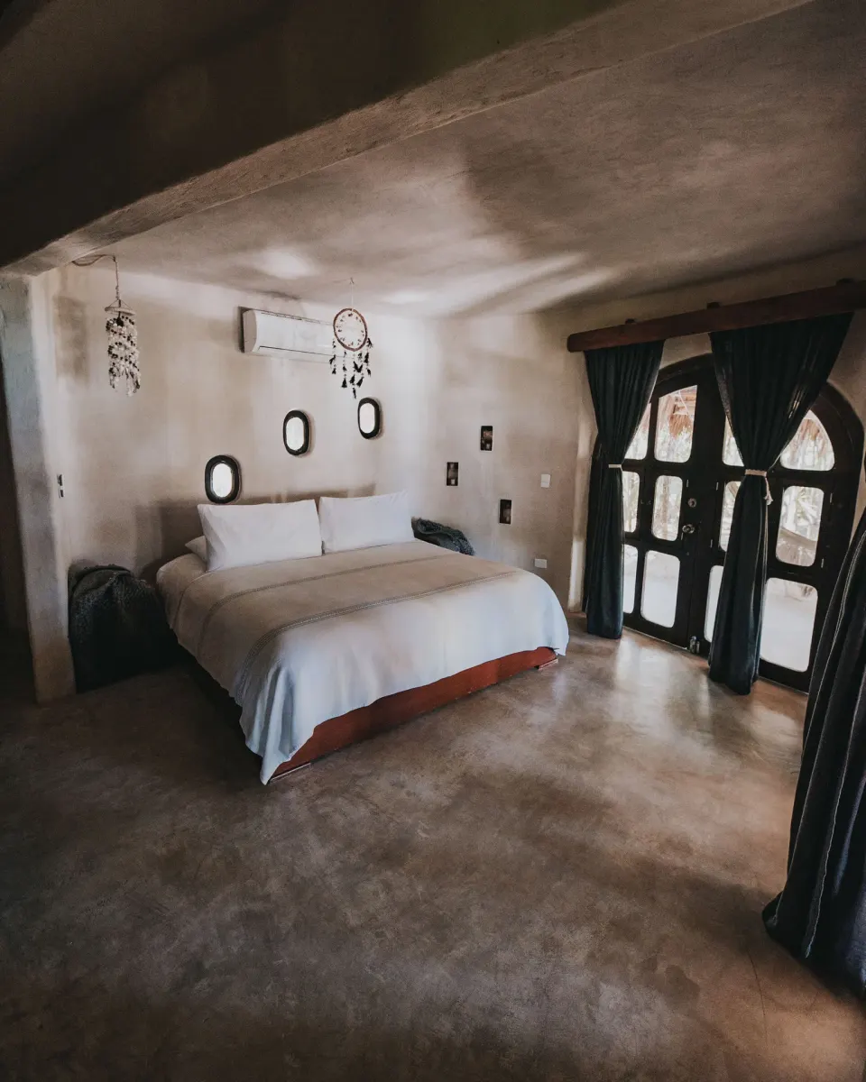 King bed with white linens and arched wooden doors in Casa Viento at Papaya Playa Project